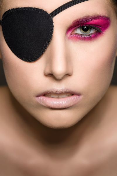 Beauty photography of makeup on a girl, in colors red or magenta, wearing an eye patch.